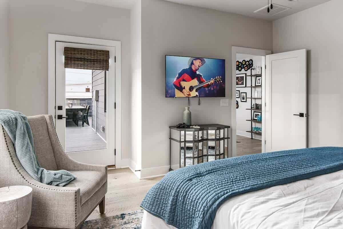 A bedroom with a bed, a chair, a TV, and a door leading to a balcony.