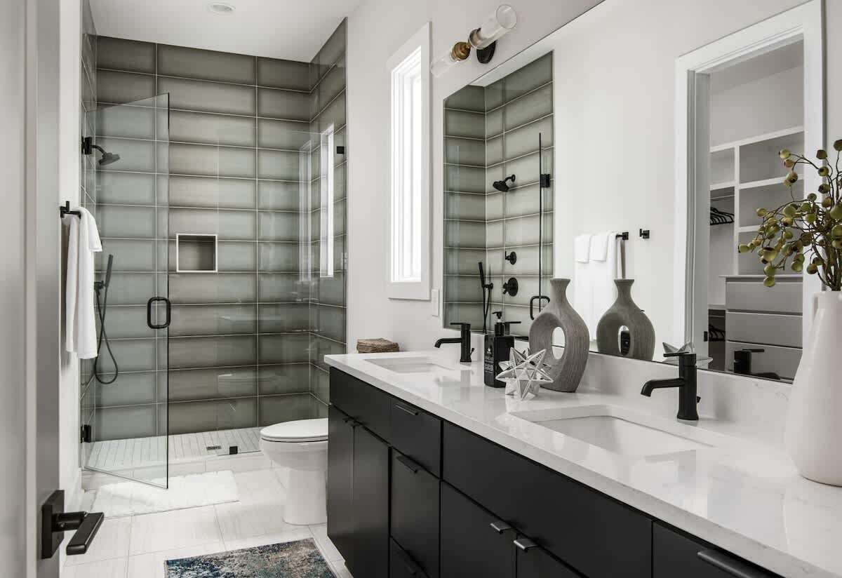 Een moderne badkamer met een douchecabine van glas, een wit wastafeltje en een grote spiegel.