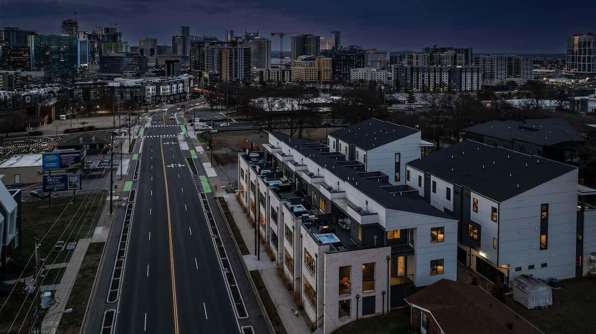 A modern urban area with a wide road, multi-story buildings, and a distant city skyline.