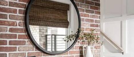 A brick wall with a round mirror, a console table with a vase, and a staircase.