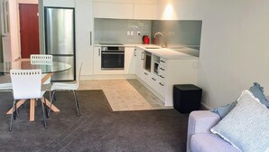 Een moderne keuken met witte kasten, een ingebouwde oven en een roestvrijstalen koelkast. Er is een eethoek met een glazen tafel en witte stoelen.