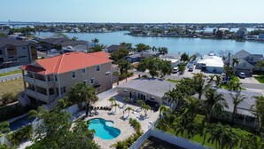 A residential area with a swimming pool, houses, and a marina in the background. - Bungalow by the Beach – Private Pool, Outdoor Lounge, Walk to Sand & Family-Friendly Backyard (Indian Rocks Beach)