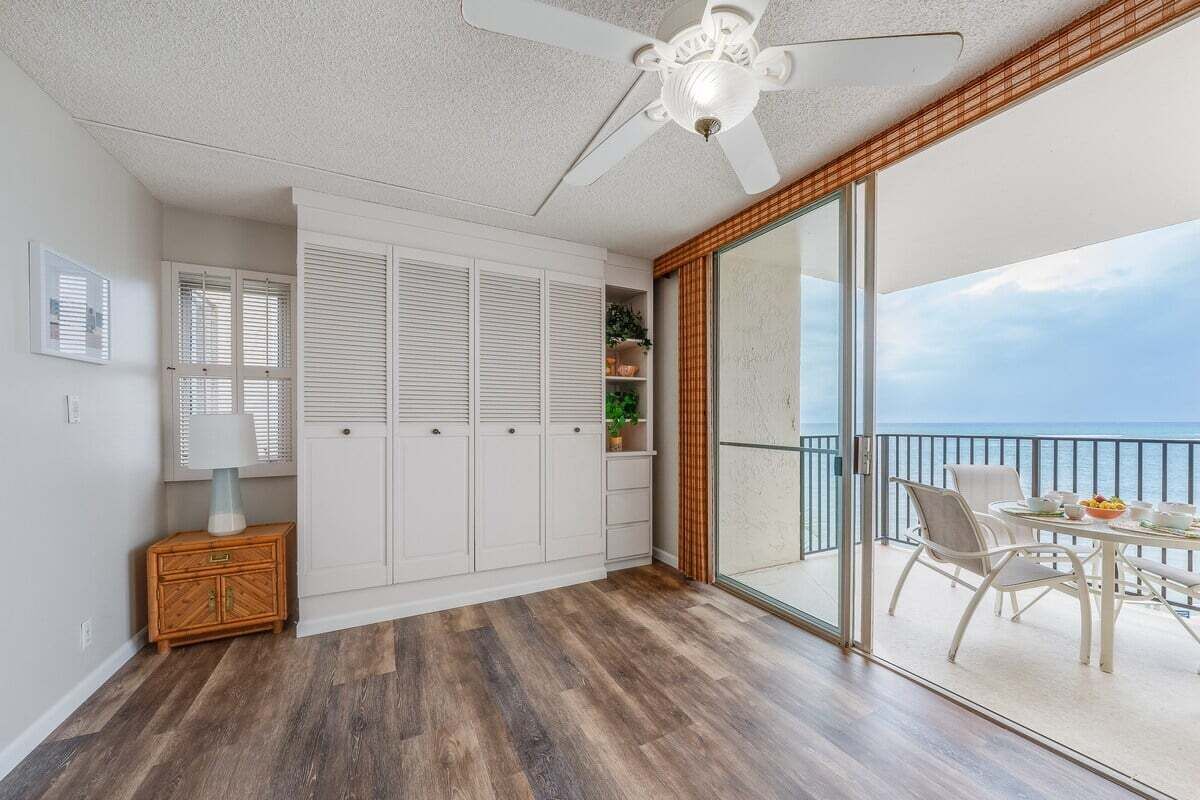 Une chambre avec un balcon, un ventilateur de plafond, une armoire en bois et une vue sur l’océan.