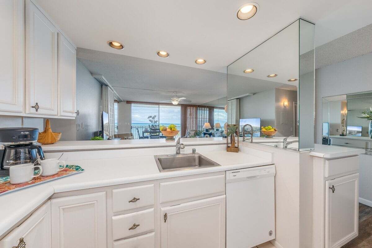 A modern kitchen with white cabinetry, a built-in dishwasher, and a large window offering a view of the outdoors.