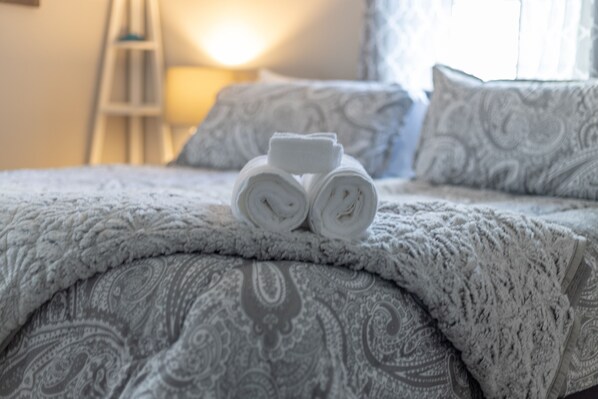 A neatly made bed with rolled white towels and a patterned blanket.