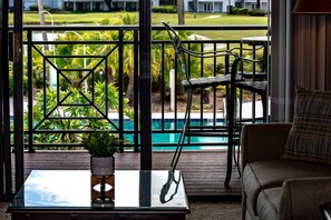 Un balcón con vista a la piscina, una mesa de vidrio, una silla y un sofá.
