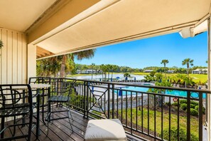 Un balcón con vista a la piscina, mobiliario exterior y cielo despejado.