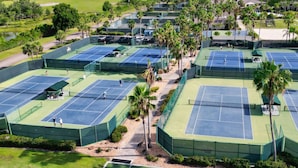 Luftaufnahme einer Tennisanlage mit mehreren Plätzen, umgeben von Grünflächen und Palmen.