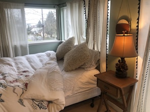 Ein Schlafzimmer mit einem Bett, einem Nachttisch mit Lampe und einem Fenster mit Vorhängen.