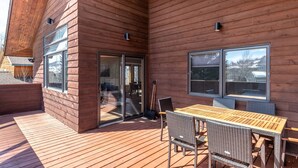 Een houten terras met een tafel en stoelen, een schuifpui en een uitzicht op een huis op de achtergrond.