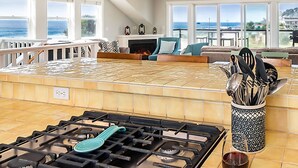 A kitchen with a gas stove, a blue spatula, and a glass of red wine on the counter.