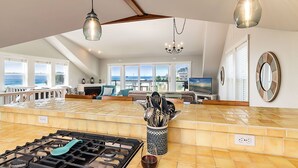 A spacious kitchen with a large island, a gas stove, and a view of the ocean through large windows.