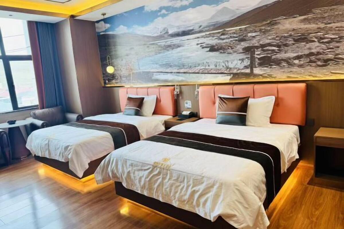 A hotel room with two beds, a large window, and a mountain landscape mural on the wall.