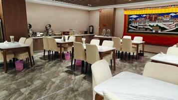 A hotel dining area with tables and chairs, a counter with a coffee machine, and a large tapestry on the wall.
