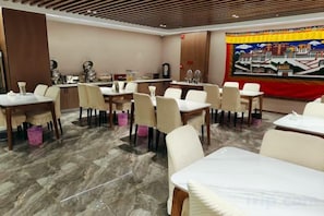A hotel dining area with tables and chairs, a counter with a coffee machine, and a large tapestry on the wall. - Naqu Zangdi Tianxiang Hotel (Nagqu)
