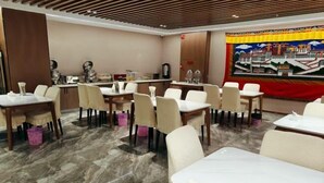 A hotel dining area with multiple tables and chairs, a marble floor, and a large tapestry on the wall.