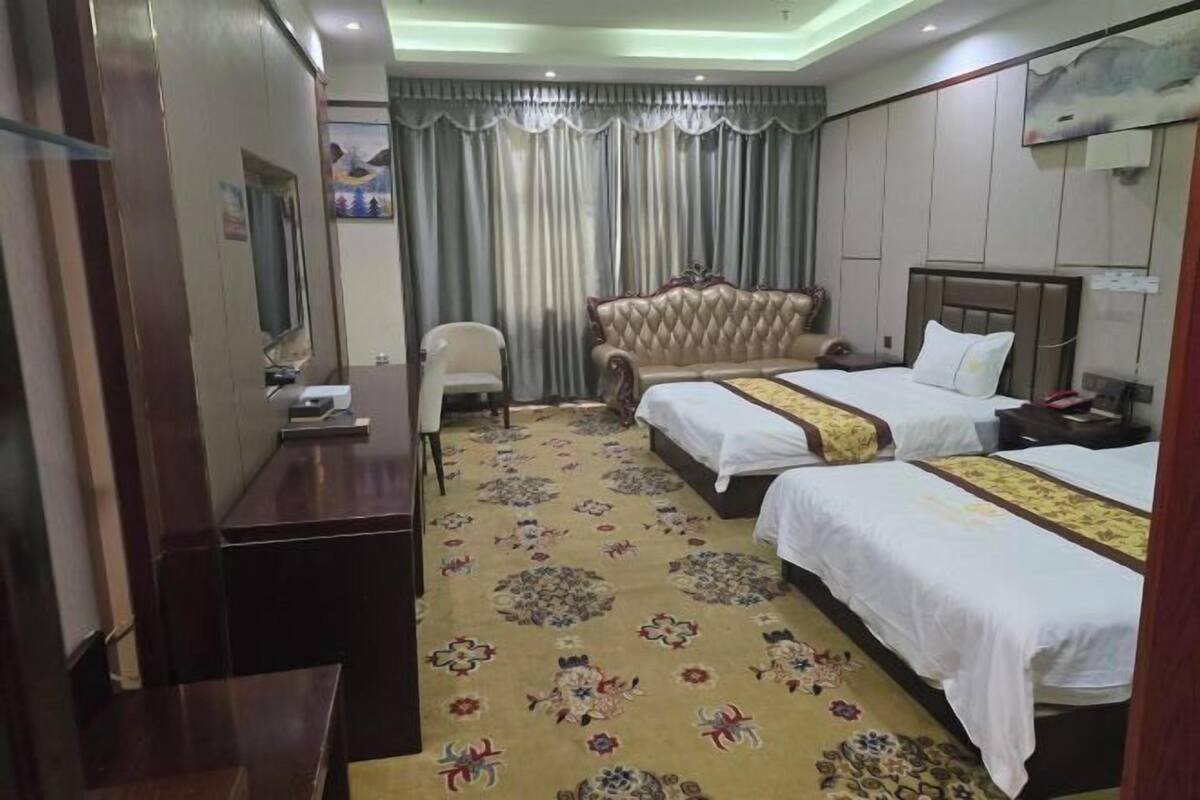 A hotel room with two beds, a sofa, a TV, and a desk.