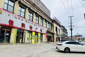 Vista de la calle con un edificio que presenta un letrero grande con caracteres chinos, un coche blanco estacionado al frente y un cielo despejado.