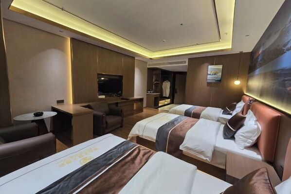 A hotel room with two beds, a desk, a TV, and a seating area.