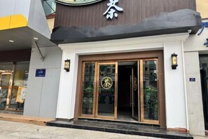 A hotel entrance with a prominent sign, a glass door, and a small outdoor seating area visible through the entrance.