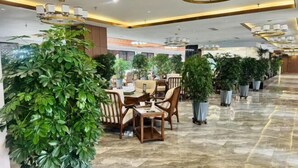 A spacious lobby with a marble floor, modern chandeliers, and multiple seating areas with potted plants.