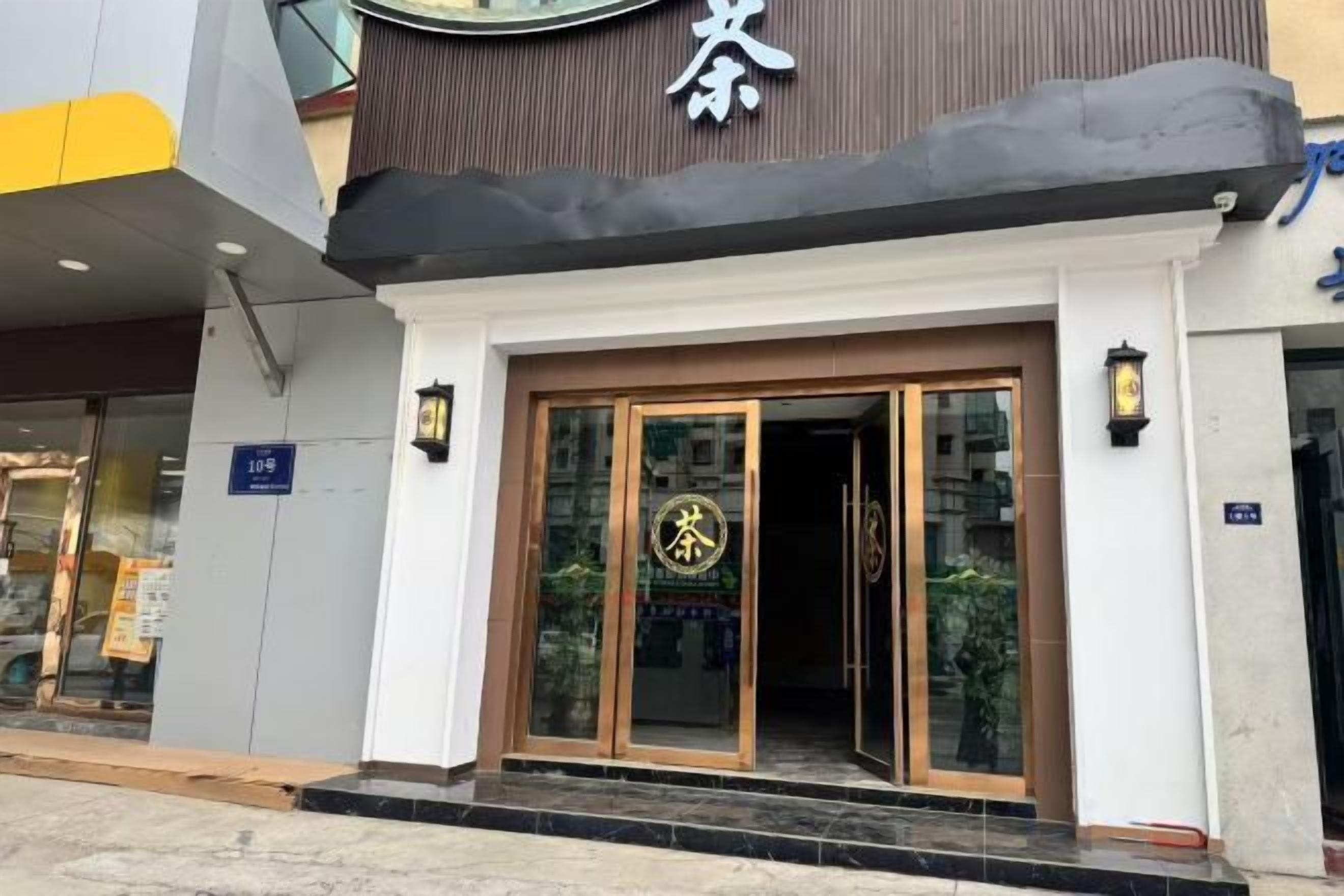 L’entrée d’un hôtel au design moderne, avec une porte en verre ornée d’un logo, un auvent noir et une enseigne indiquant l’entrée.