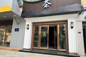 A hotel entrance with a modern design, featuring a glass door with a logo, a black awning, and a sign indicating the entrance.