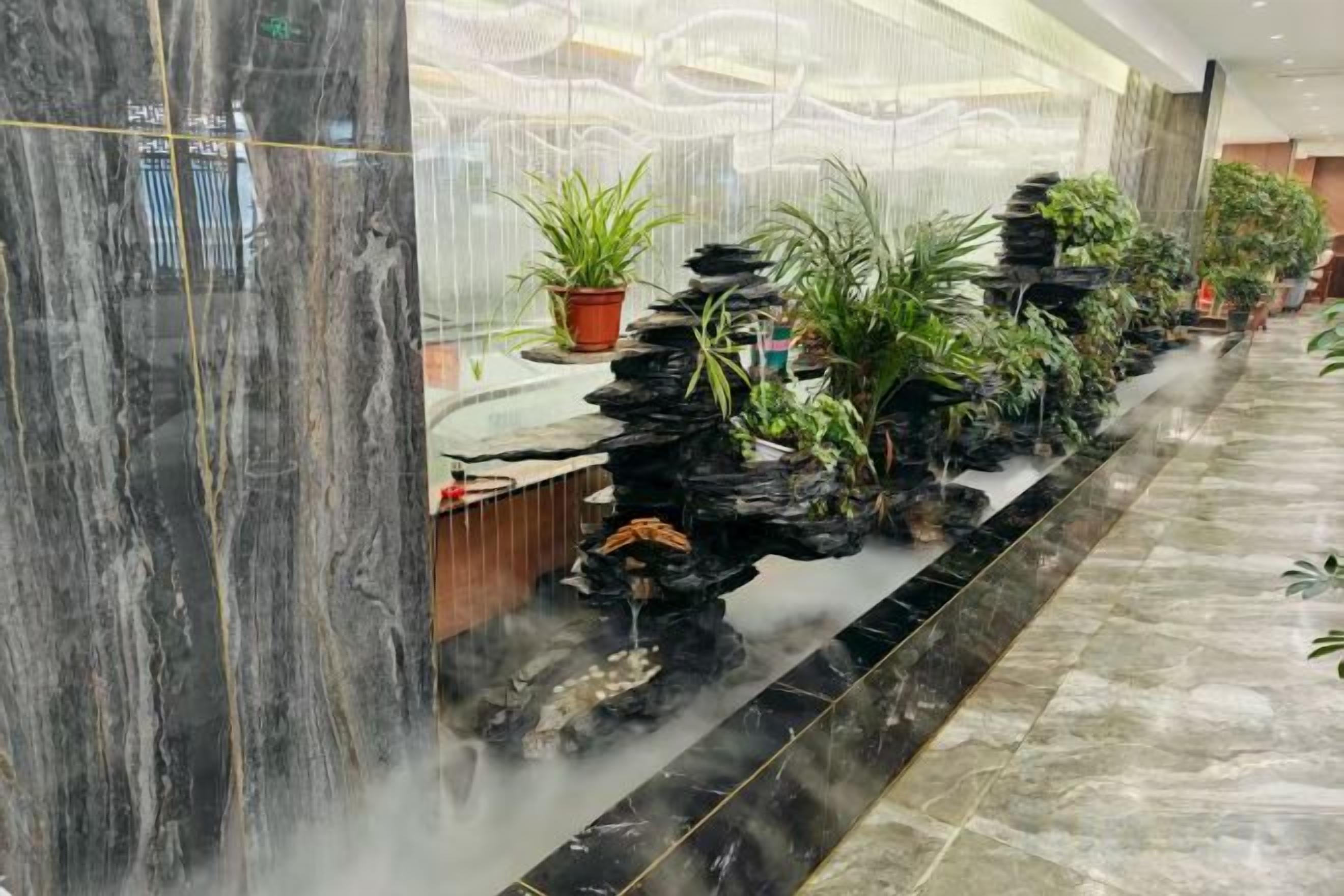 A lobby with a water feature, marble columns, and potted plants.