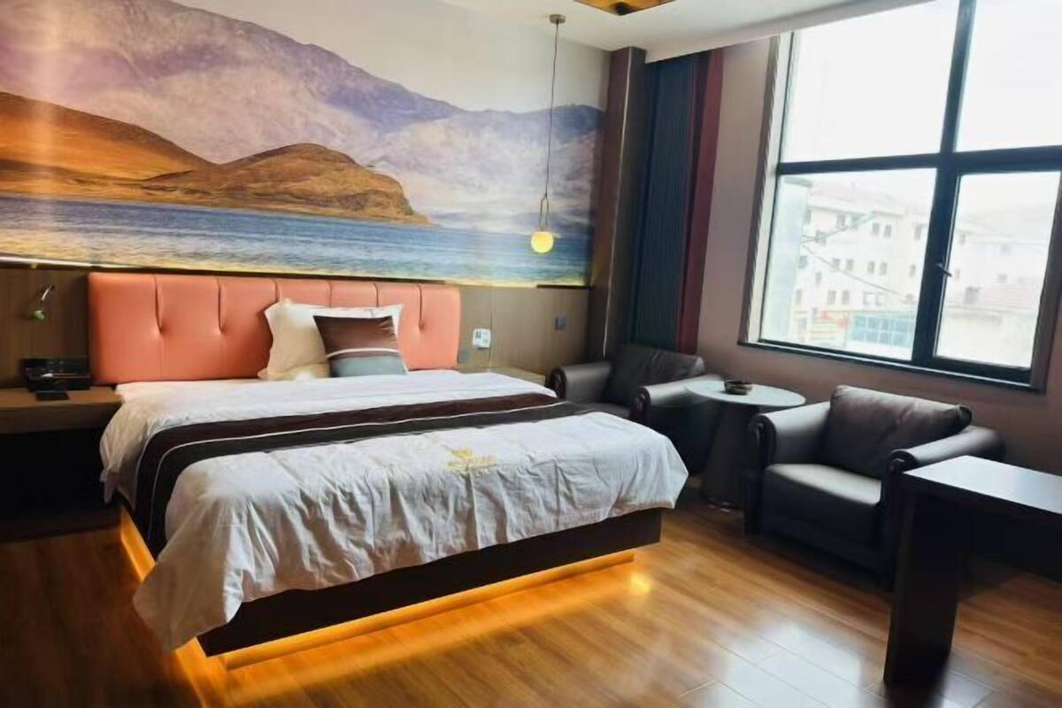 A hotel room with a bed, a sofa, a small table, a lamp, and a large window with a view of buildings.