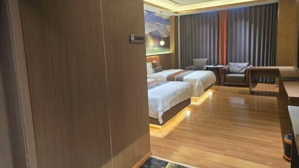 A hotel room with a wooden floor, two beds with white linens, a sofa, a small table, and a wall-mounted TV. - Naqu Zangdi Tianxiang Hotel (Nagqu)