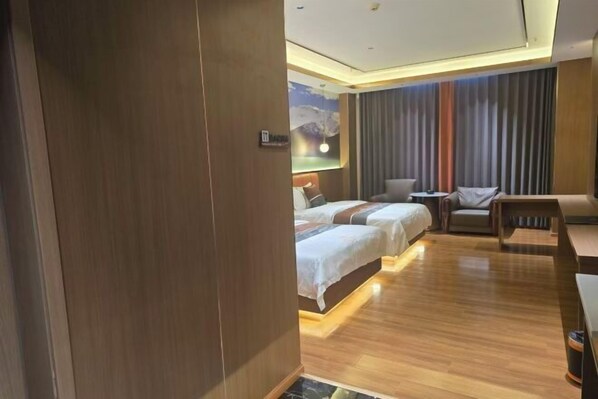 A hotel room with a wooden floor, two beds with white linens, a sofa, a small table, and a wall-mounted TV.