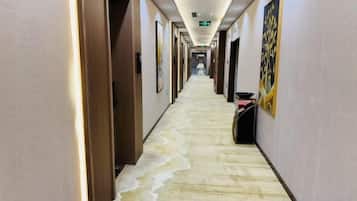 A hotel corridor with doors on the left, a carpeted floor, and framed artwork on the walls.