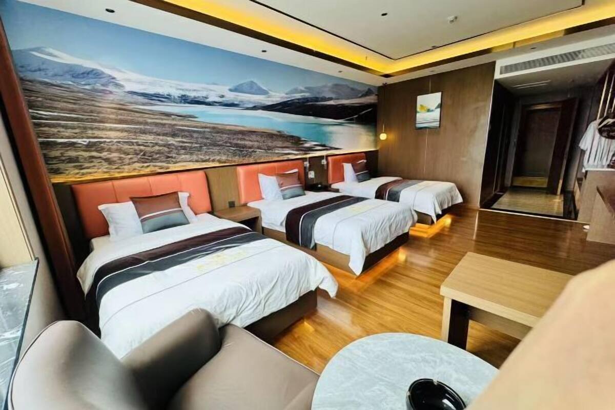 A hotel room with two beds, a sofa, a small table, and a large mural of a mountainous landscape.