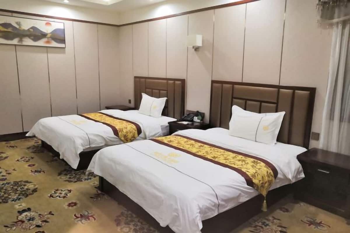 A hotel room with two beds, each with a wooden headboard, white bedding, and a floral-patterned bed runner.