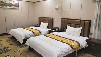 Habitación de hotel con dos camas, cada una con cabecera de madera, ropa de cama blanca y un corredor de cama estampado con motivos florales.
