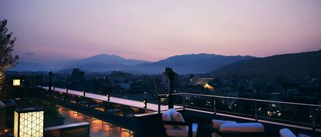 Una terraza en la azotea con mobiliario exterior, una chimenea y vistas a la ciudad al atardecer.