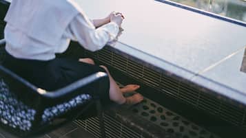 Une personne assise sur un banc muni d’une rambarde en métal, portant un chemisier blanc et une jupe noire.