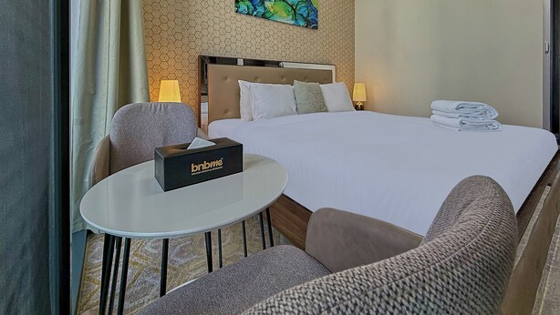 Una habitación de hotel con una cama, una mesita de noche con un dispensador de pañuelos, una silla, una lámpara y un cuadro en la pared.