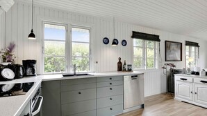 Une cuisine moderne avec un lambris en bois blanc, un grand îlot central doté de tiroirs gris, un four encastré et une fenêtre donnant sur un paysage verdoyant.