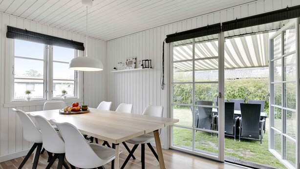 Un espace repas avec une grande table, des chaises blanches et une vue sur l’extérieur.