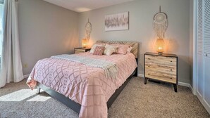 A bedroom with a bed, two nightstands, a ceiling fan, a wall-mounted dreamcatcher, and a window with curtains. - Oak Island Getaway w/ Yard - Walk to Beach! (Oak Island)