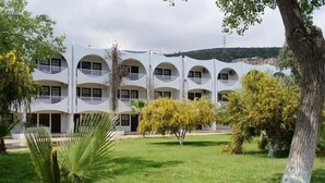 Un edifici de diverses plantes amb balcons, envoltat d'un jardí ben cuidat i arbres.