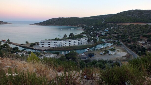 A coastal hotel with multiple floors, a marina with boats, and a hilly backdrop.