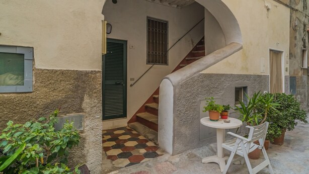 A narrow courtyard with a tiled floor, a white table with chairs, and potted plants. - BILOCALE NEL CENTRO DI PORTOFERRAIO (Portoferraio)