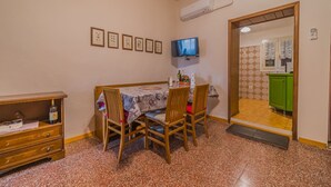 A dining area with a table set for four, a television mounted on the wall, and a kitchen visible through an open doorway. - BILOCALE NEL CENTRO DI PORTOFERRAIO (Portoferraio)