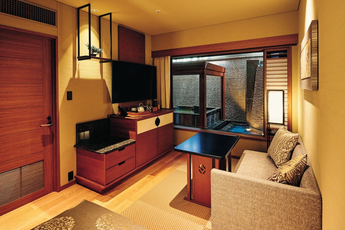 Une chambre d’hôtel compacte dotée d’une kitchenette, d’un canapé, d’une petite table et donnant sur un balcon.