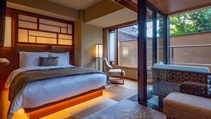 A hotel room with a large bed, a sitting area with a chair, and a view through a glass door. - Sora Niwa Terrace Kyoto (Kyoto)
