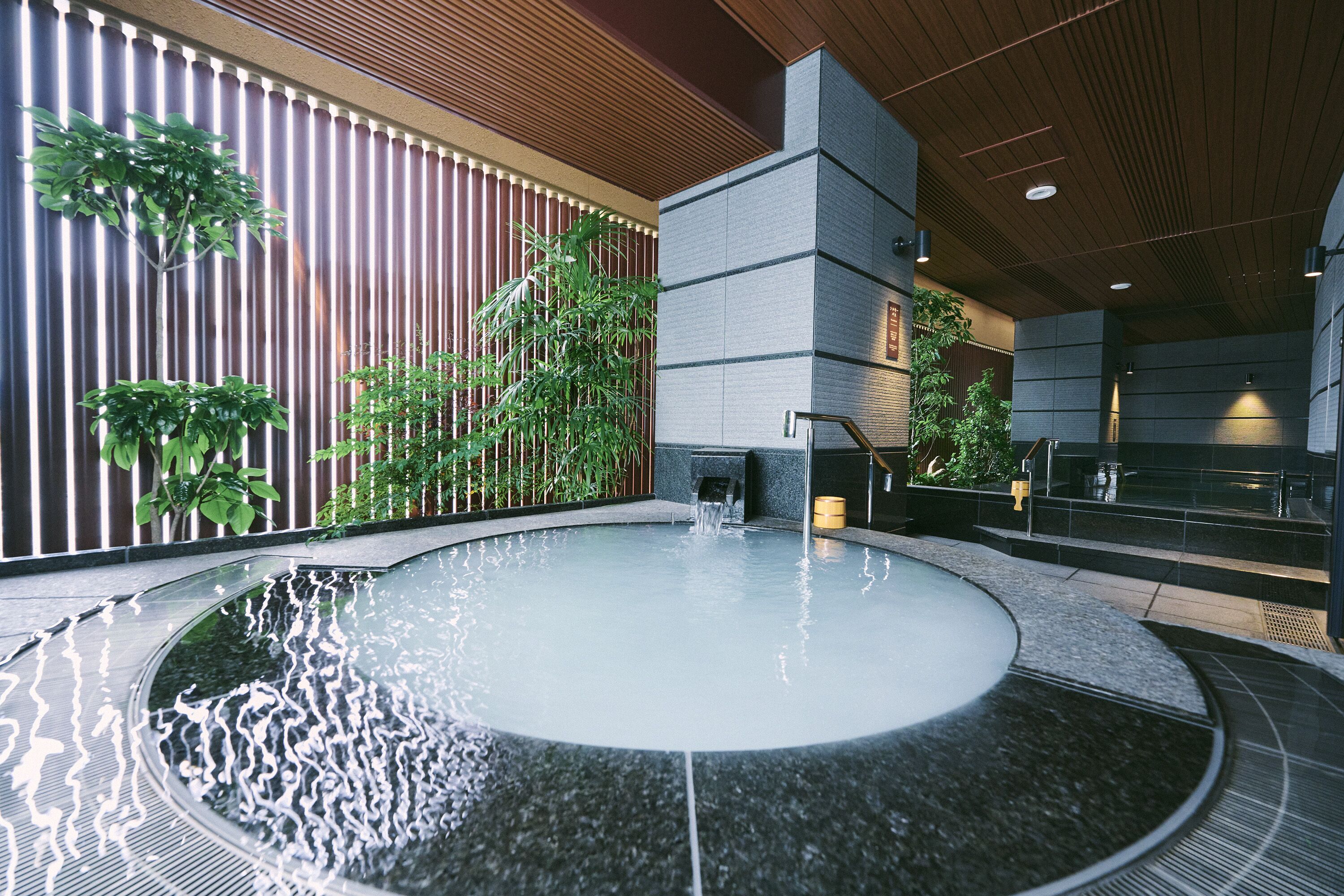 Un espace piscine intérieur moderne, doté d’un élément aquatique circulaire, entouré de panneaux de bois et de verdure.