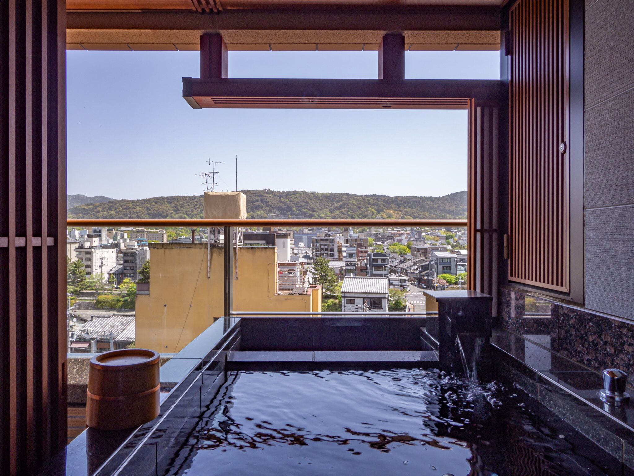 A modern bathroom with a large bathtub, a wooden barrel, and a view of a cityscape through a large window.