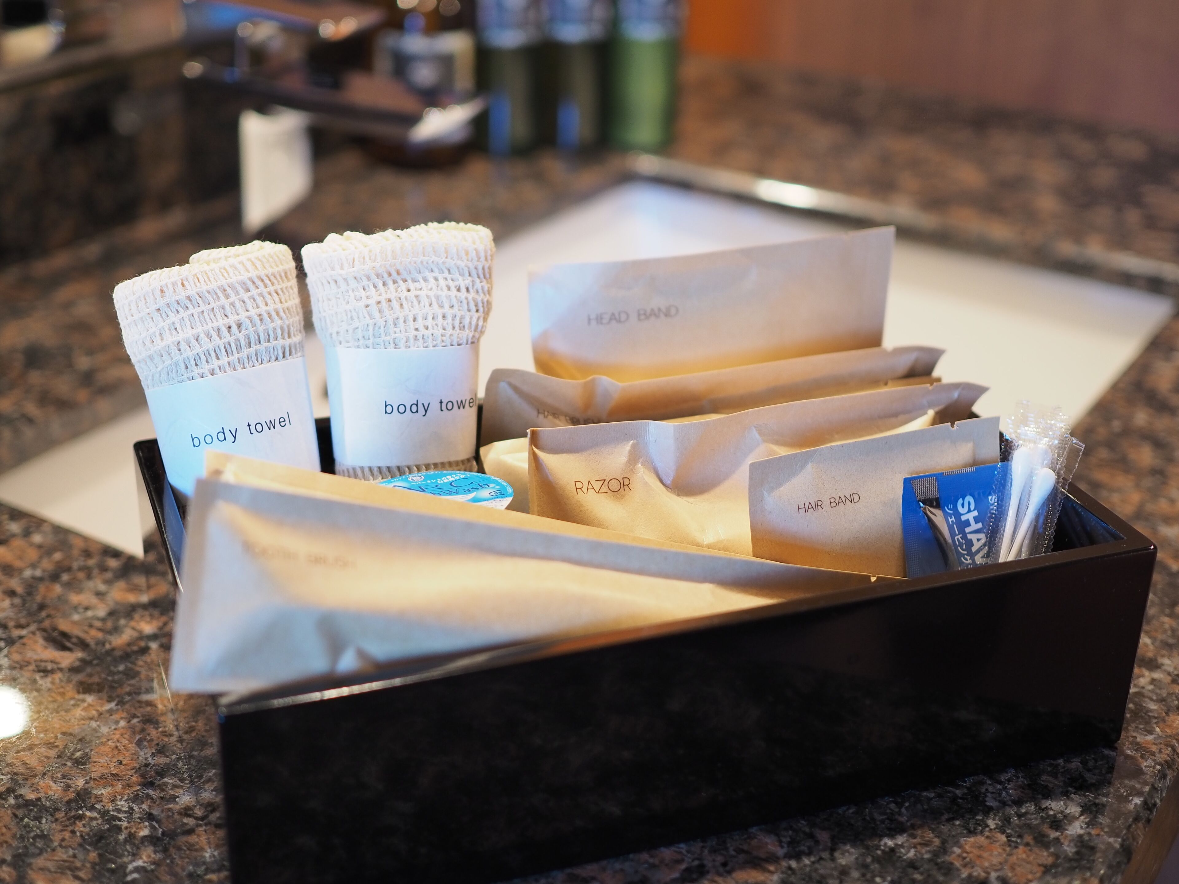 Un plateau contenant divers articles de toilette, notamment des serviettes de bain, un rasoir et un élastique à cheveux.